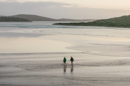 Two people walking in the shallow water of an inlet on a winters day - Australian Stock Image