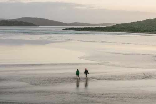 Two people walking in the shallow water of an inlet on a winters day