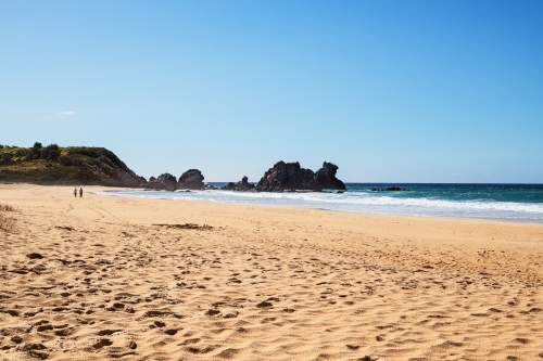 Two people walking on beach towards Camel Rock - Australian Stock Image