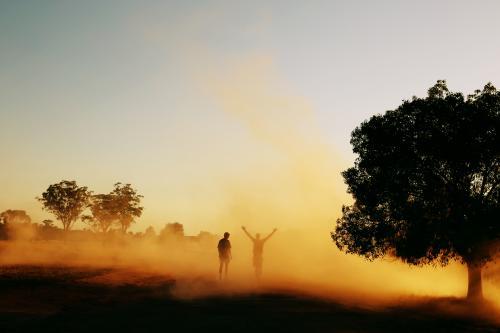 Two people walking through dust in the country.