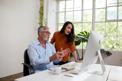 Two professional business people, sharing ideas in an open-plan studio office - Australian Stock Image