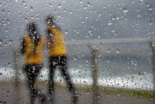 Two runners wearing yellow jackets in the rain seen through a window with water drops on it