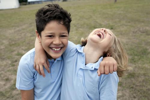 Two school kids laughing outside with arm around each other