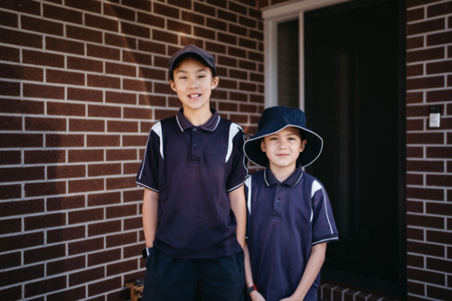 Two siblings standing outside of their house in uniform ready for school - Australian Stock Image