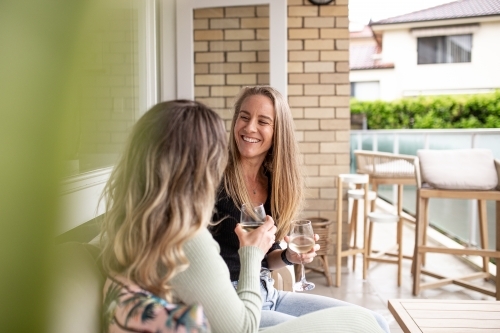 Two smiling women sitting outside looking at eachother while holding a champagne glass