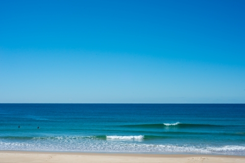 Two surfers waiting for a wave on a flat beach - Australian Stock Image