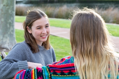 two teen girls sitting on park bench together - Australian Stock Image