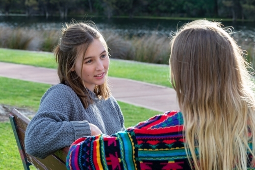 two teen girls sitting on park bench together - Australian Stock Image