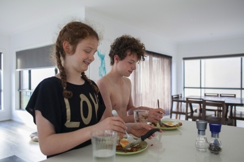 Two teenage children eating breakfast at home