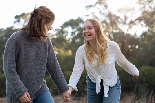 two teenage girls holding hands in natural setting - Australian Stock Image