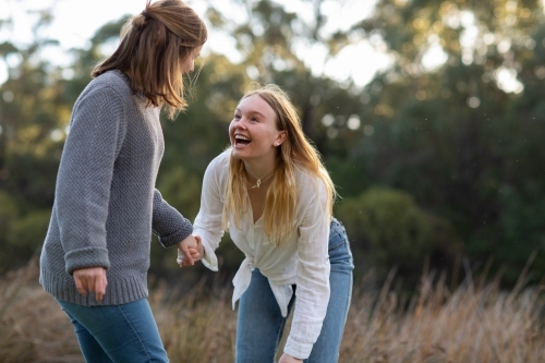 two teenage girls holding hands in natural setting - Australian Stock Image