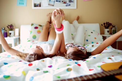 Two teenage girls lying on a bed holding hands