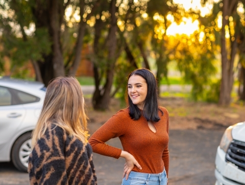 two teenagers outside near vehicles with trees in background - Australian Stock Image