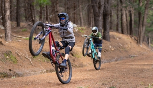 two teenagers wearing full face helmets doing wheelies on their mountain bikes on trail - Australian Stock Image