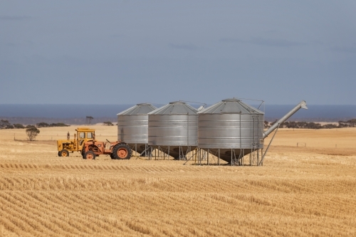 Two tractors & three metal grain silos in a patterned, harvested field
