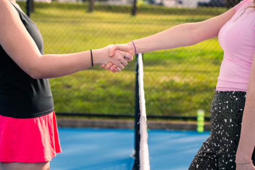 Two women shaking hands over tennis net on outdoor court - Australian Stock Image