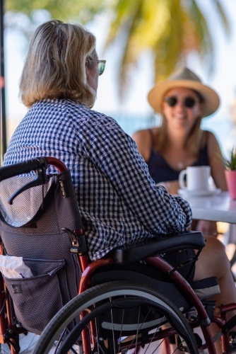 two women sitting at cafe with palm tree in background - Australian Stock Image