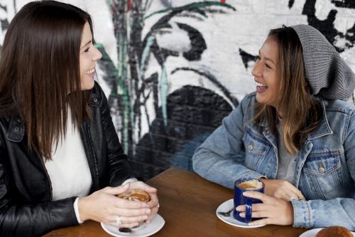 Two women smiling and laughing with each other at a cafe - Australian Stock Image