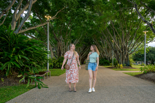 Two women walking side by side along a tree-lined pathway in a lush park - Australian Stock Image