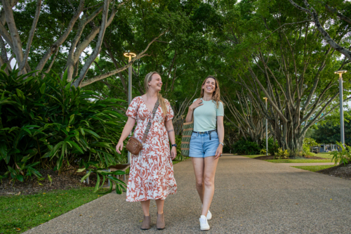 Two women walking side by side along a tree-lined pathway in a lush park - Australian Stock Image