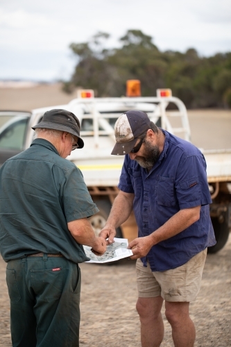 two working men in the country looking at a map outdoors - Australian Stock Image