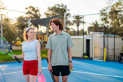 Two young adults walking on a tennis court after a tennis match, enjoying the warm sunset - Australian Stock Image