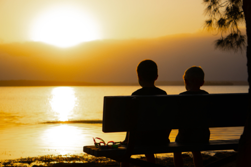 Two young boys at sunset on a park bench - Australian Stock Image