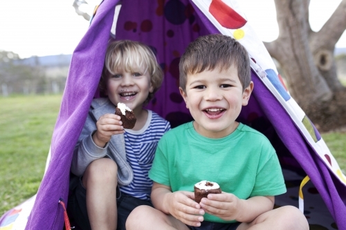 Two young boys eating cupcakes and smiling looking straight into the camera