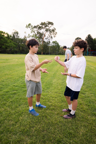 Two young boys Playing Rock‑Paper‑Scissors in a green grassy soccer field - Australian Stock Image