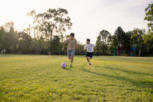 Two young boys playing soccer on a grassy field at sunset - Australian Stock Image