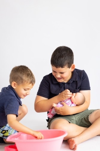 two young boys playing with a baby doll and baby bath - Australian Stock Image
