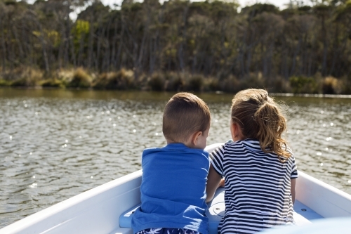 Two young children sitting in a row boat on the water