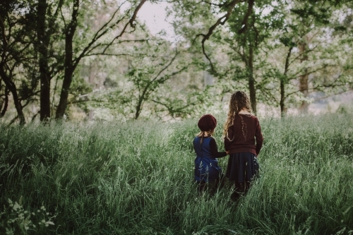 Two young fashionable sisters walking through a lush green paddock of long grass - Australian Stock Image