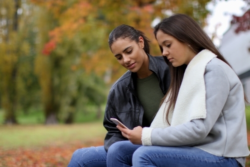 Two young female friends sitting together in an outdoor setting - Australian Stock Image