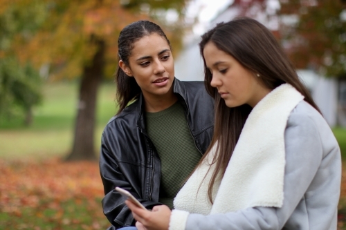 Two young female friends sitting together in an outdoor setting - Australian Stock Image