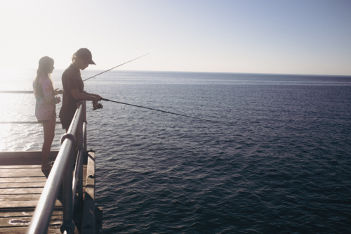 Two young female teenagers fishing from Jetty into calm water - Australian Stock Image