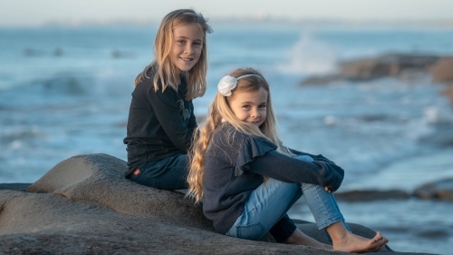 Two young girls sitting on rock at beach