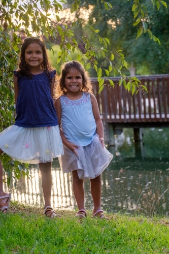 Two young girls standing on the grassy embankment of a dam in parkland - Australian Stock Image