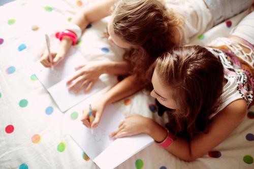 Two young girls writing on a bed