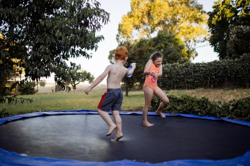 Two young kids having a water fight on a trampoline