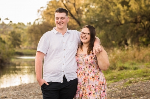 Two young people dating holding hands laughing as they look out over water - Australian Stock Image