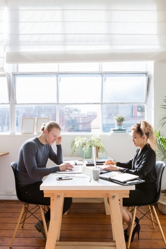 Two young people working at a shared desk - Australian Stock Image