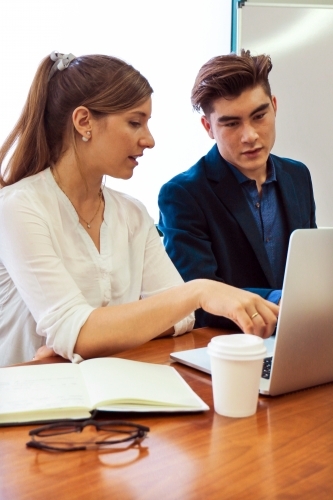 Two young professional office workers sitting at a meeting table with laptop - Australian Stock Image