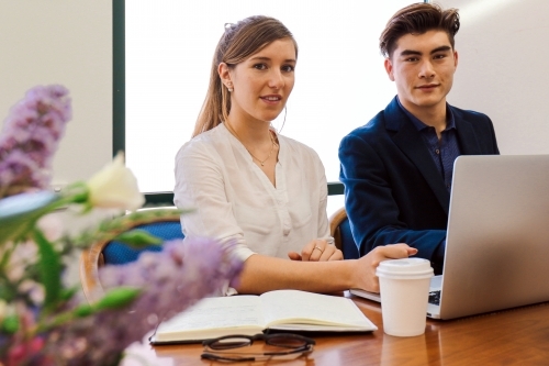 Two young professional office workers sitting at a meeting table with laptop - Australian Stock Image