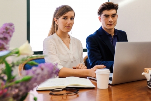 Two young professional office workers sitting at a meeting table with laptop
