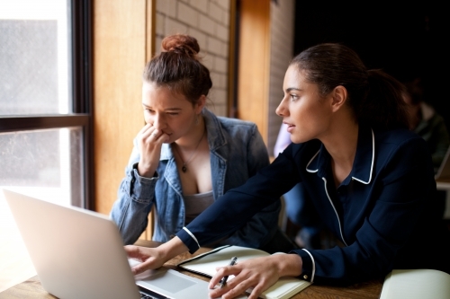 Two young women sitting at a desk in a classroom - Australian Stock Image