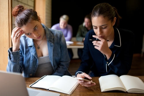 Two young women sitting at a desk in a classroom - Australian Stock Image