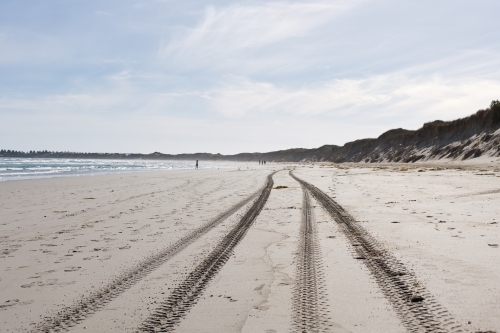tyre tracks and footprints on a beach with people in distance