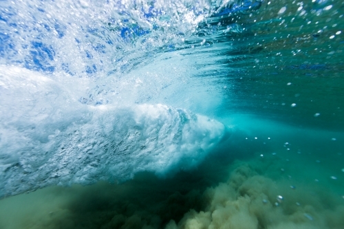 Under water view of an ocean wave breaking in a vortex on sand in crystal clear, blue water. - Australian Stock Image