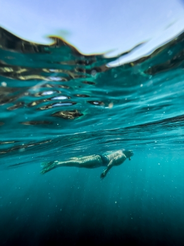 Underwater of female snorkelling in ocean afloat at surface looking down - Australian Stock Image